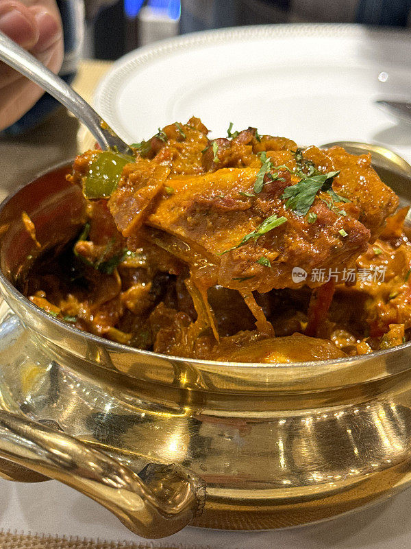 一勺辣鸡肉tikka masala咖喱的特写图像，在餐厅桌子上的金色金属碗上，餐厅设置背景，高架视图，重点放在前景上